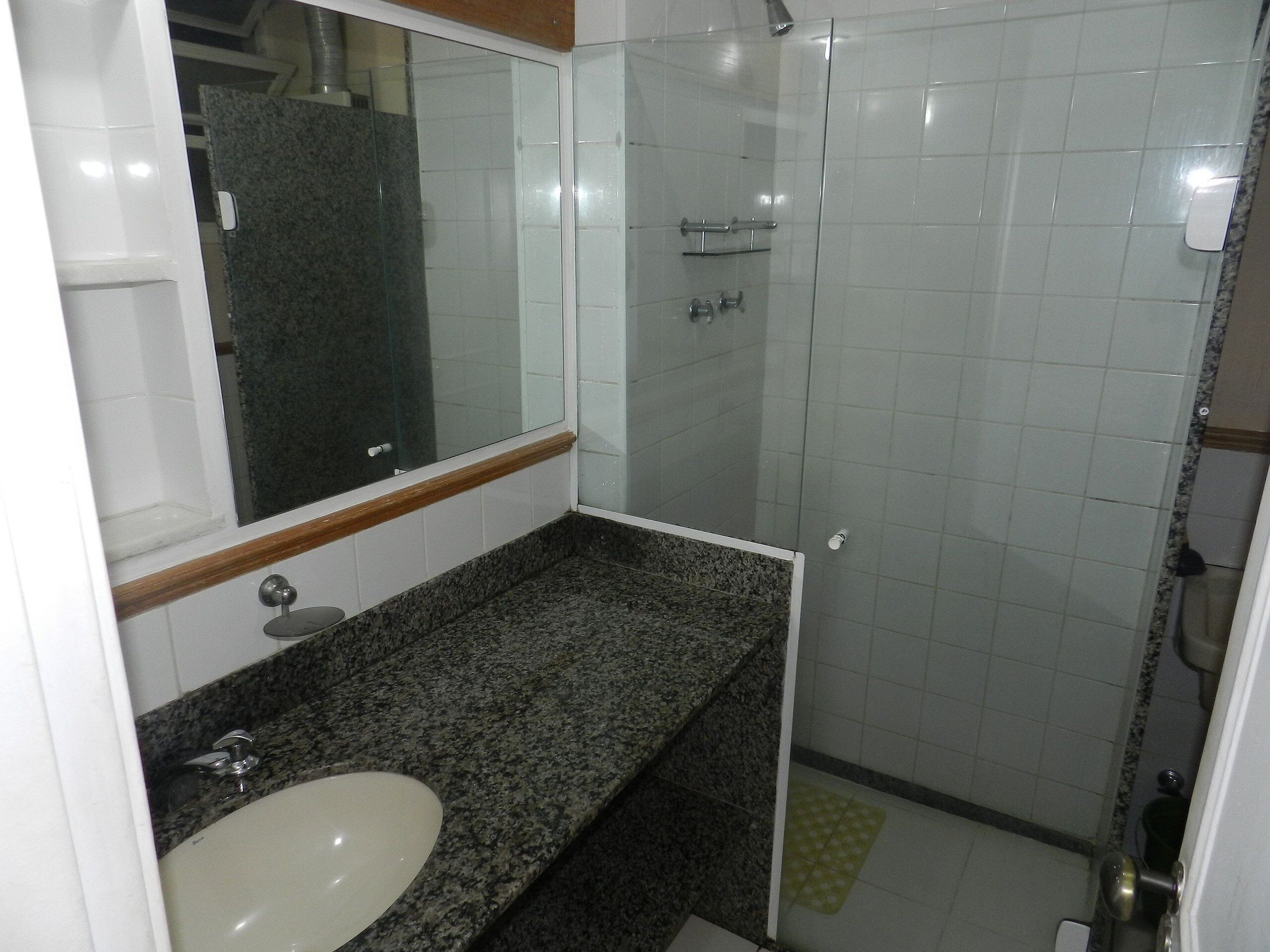 A bathroom with a granite countertop, a white sink, a mirror, and a glass-enclosed shower area.