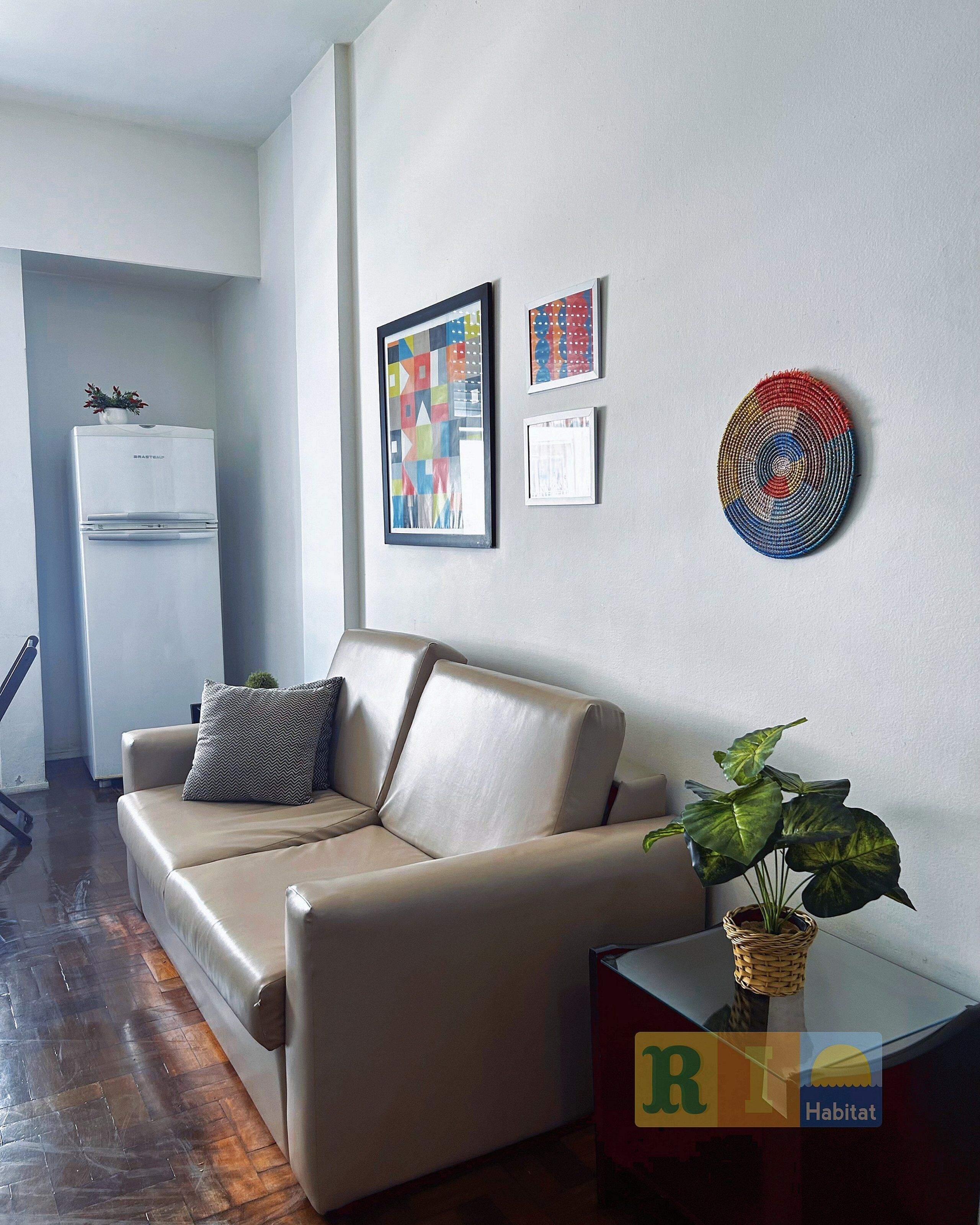 Un salón moderno con un sofá color beige, una mesita con una planta y obras de arte en la pared.