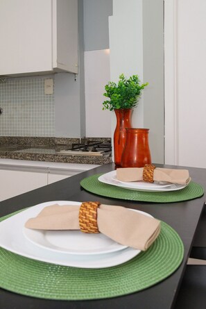 A kitchen with a granite countertop, a stove, a vase with green plants, and a neatly set table with plates and napkins. - Rio Habitat Almirante (Rio de Janeiro)