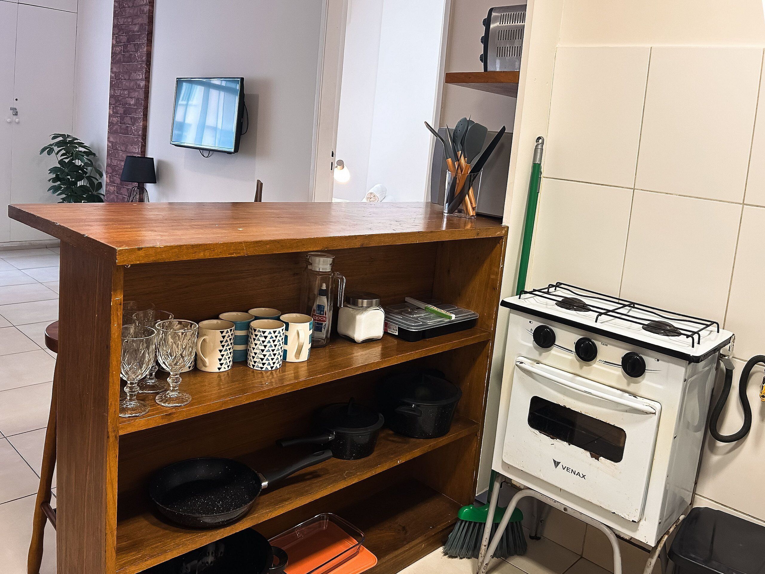 Eine Küche mit einem Holzbodenregal mit Tassen, einem Herd und einem an der Wand befestigten Fernseher.