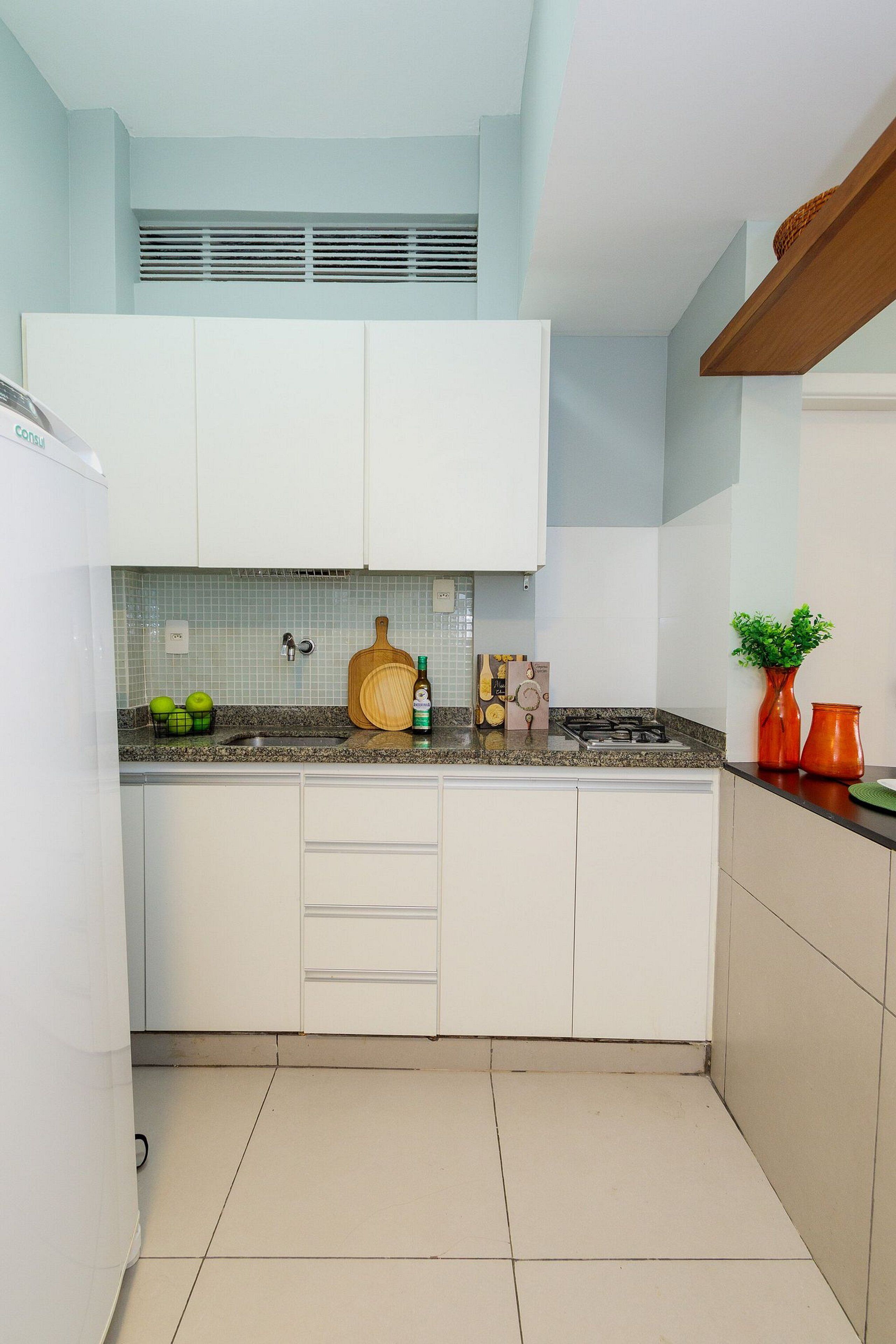 Een compacte keuken met witte kasten, een granieten aanrecht en een betegelde spatwand.