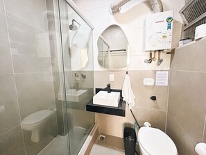 A bathroom with a glass shower enclosure, a white toilet, a sink with a black countertop, and a towel hanging on a rack. - Rio Habitat Almirante (Rio de Janeiro)