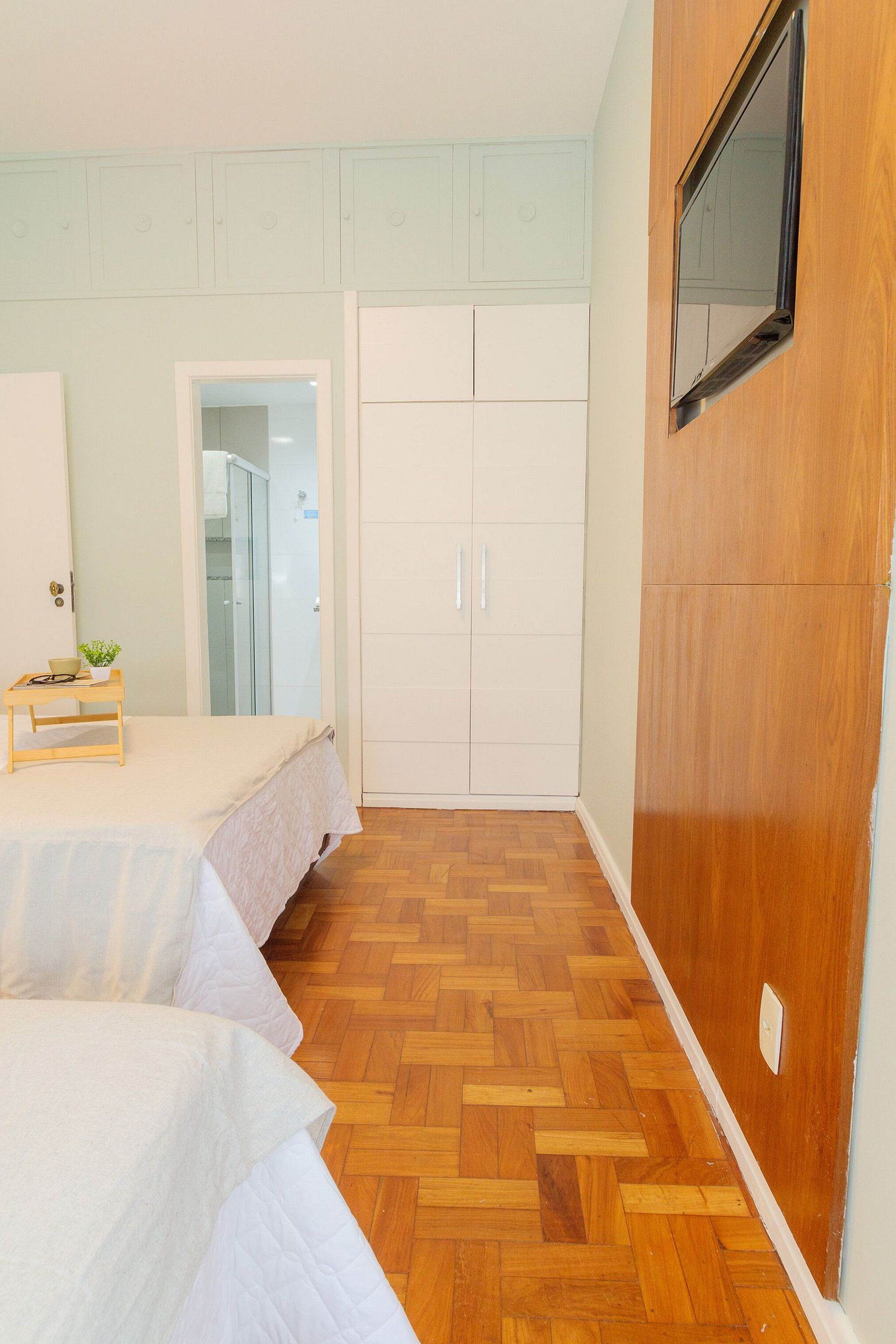 A bedroom with a bed, a wooden wardrobe, a mirror, and a small table with a bowl and plant.