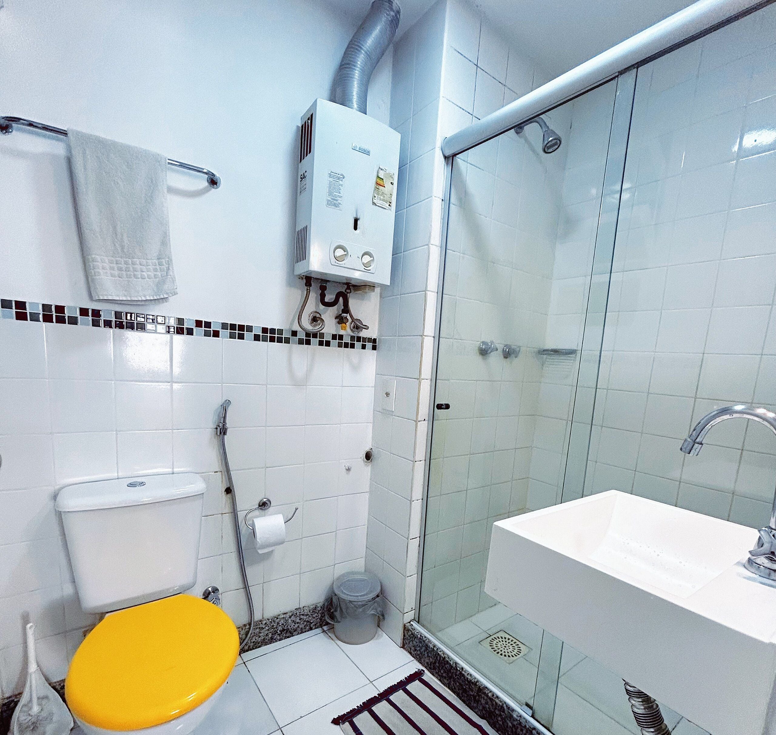 A bathroom with a toilet, sink, shower, and a Bosch water heater.
