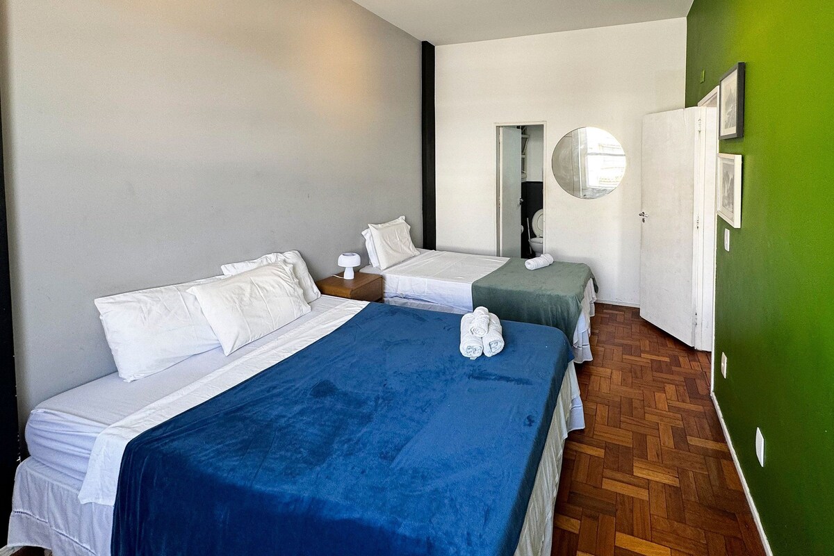 Une chambre d’hôtel avec deux lits, un miroir, un mur vert et un plancher en bois.