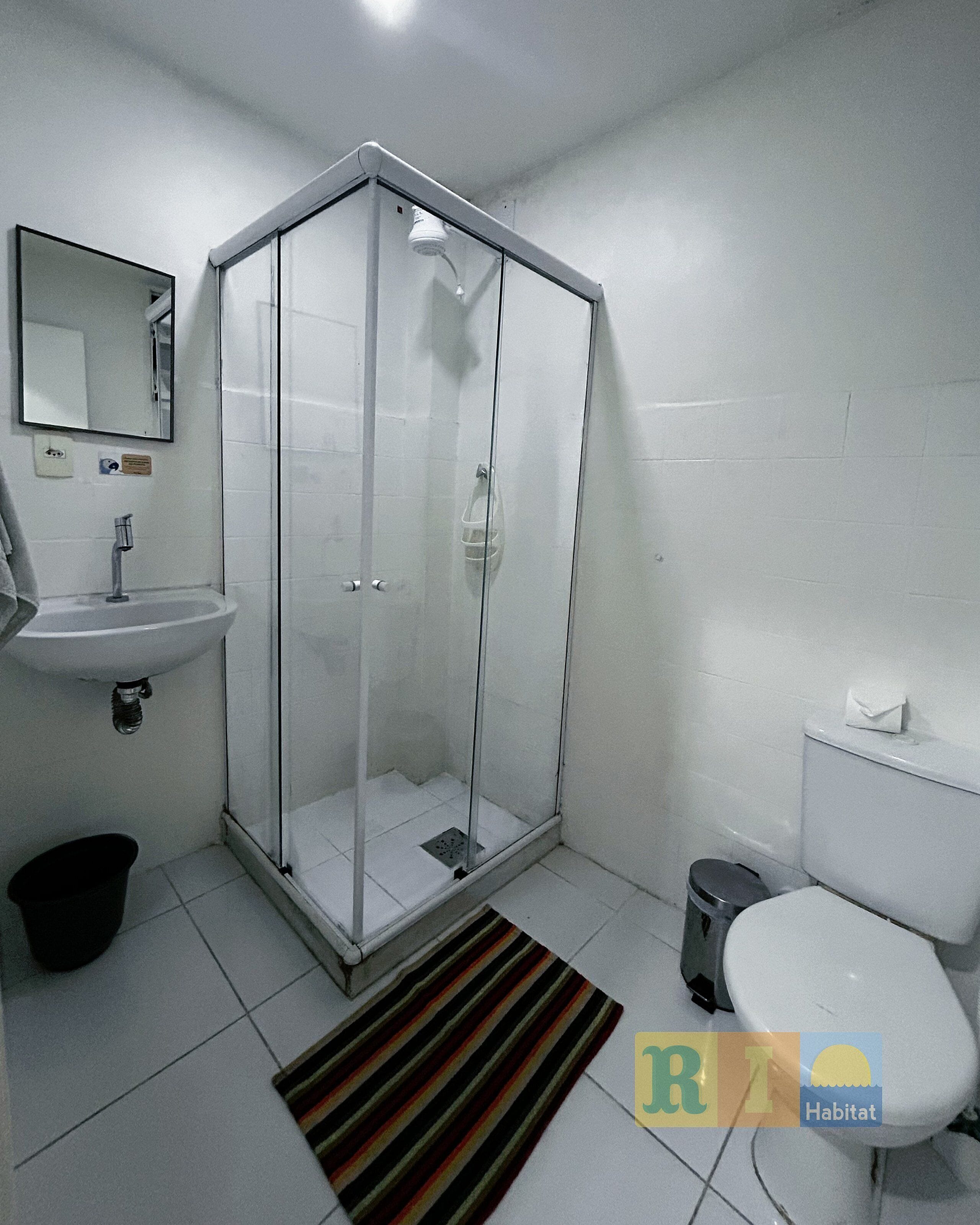 A bathroom with a glass-enclosed shower, a sink, a toilet, and a striped rug.