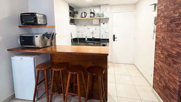A compact kitchen with a wooden countertop, two microwaves, a refrigerator, and a door leading to a bathroom. - Rio Habitat Almirante (Rio de Janeiro)