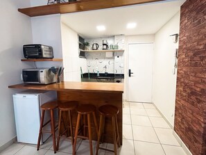 A compact kitchen with a wooden countertop, two microwaves, a refrigerator, and a door leading to a bathroom. - Rio Habitat Almirante (Rio de Janeiro)