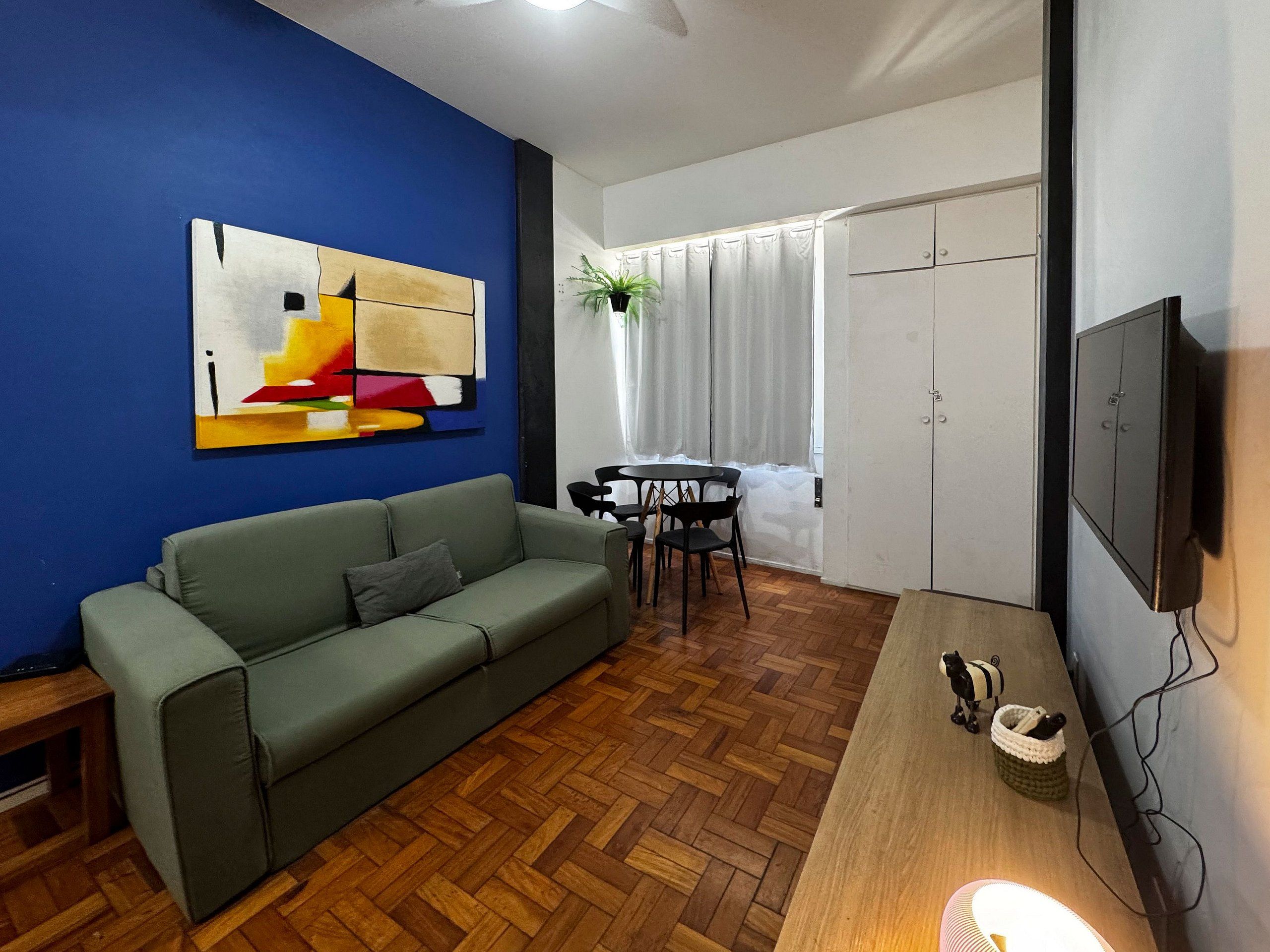 Una sala de estar con sofá, mesa de comedor, sillas, televisor y ventana con cortinas.