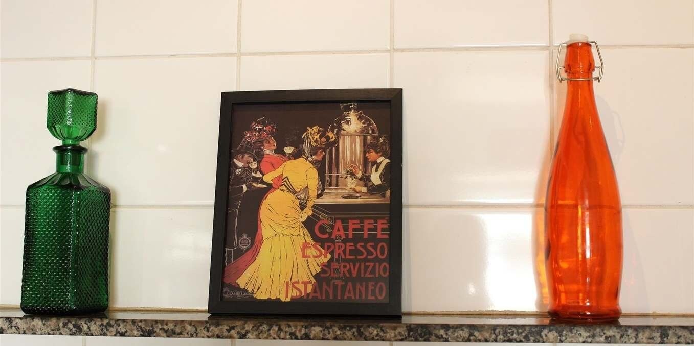 Une vieille affiche encadrée faisant la publicité d’un café, deux bouteilles et un mur recouvert de carreaux.