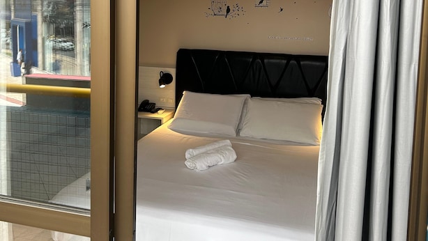 Una habitación de hotel con cama, mesita de noche, decoración en la pared y vistas por la ventana.