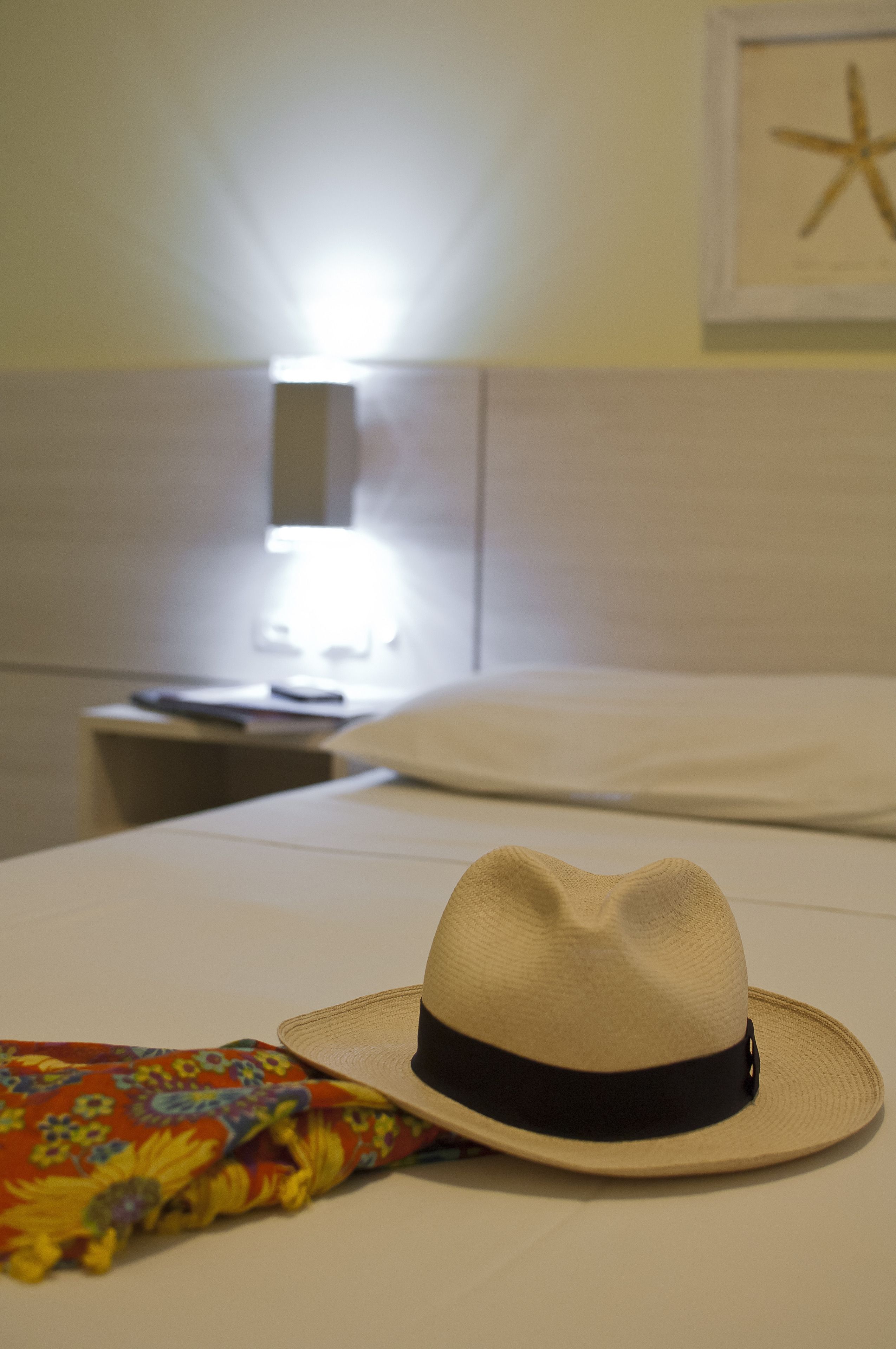 A bed with a hat and a colorful pillow, a nightstand with a lamp, and a framed picture on the wall.