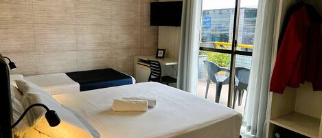 A hotel room with a bed, bedside table, lamp, and a view of the outside balcony.