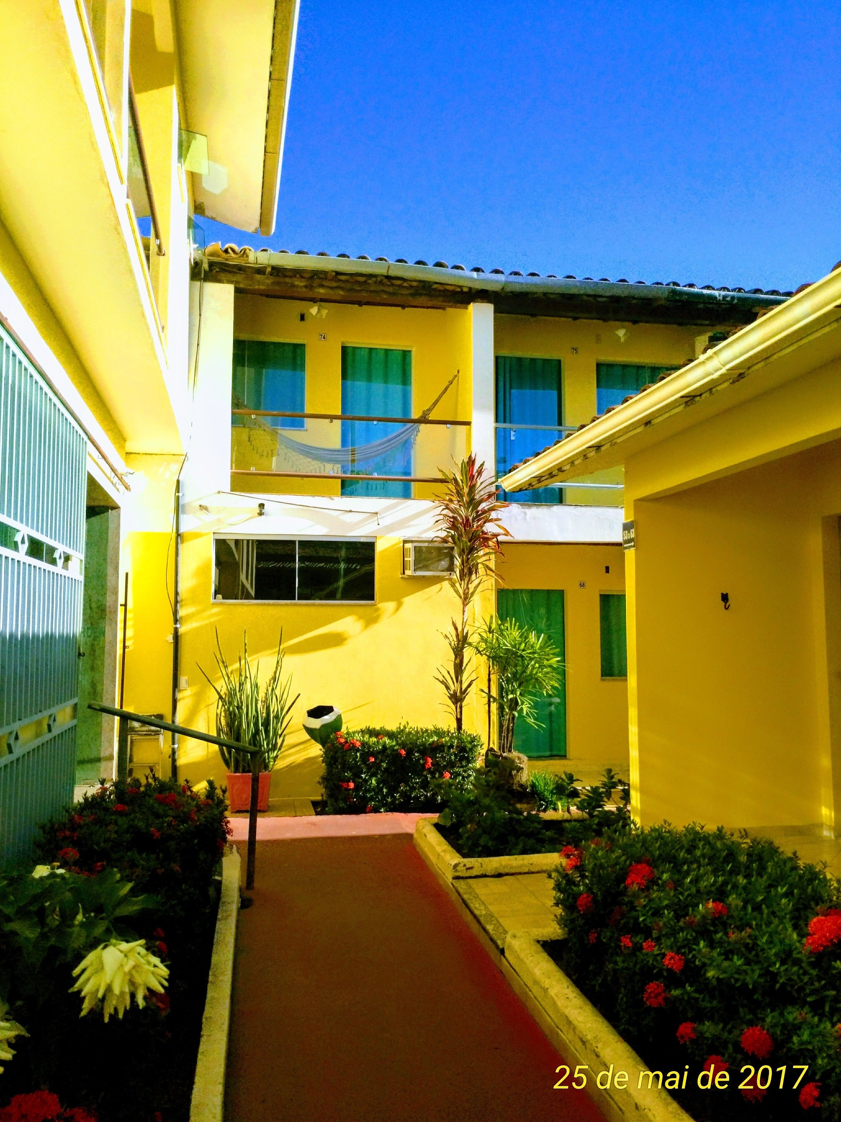 A yellow building with a red pathway, green plants, and a hammock.