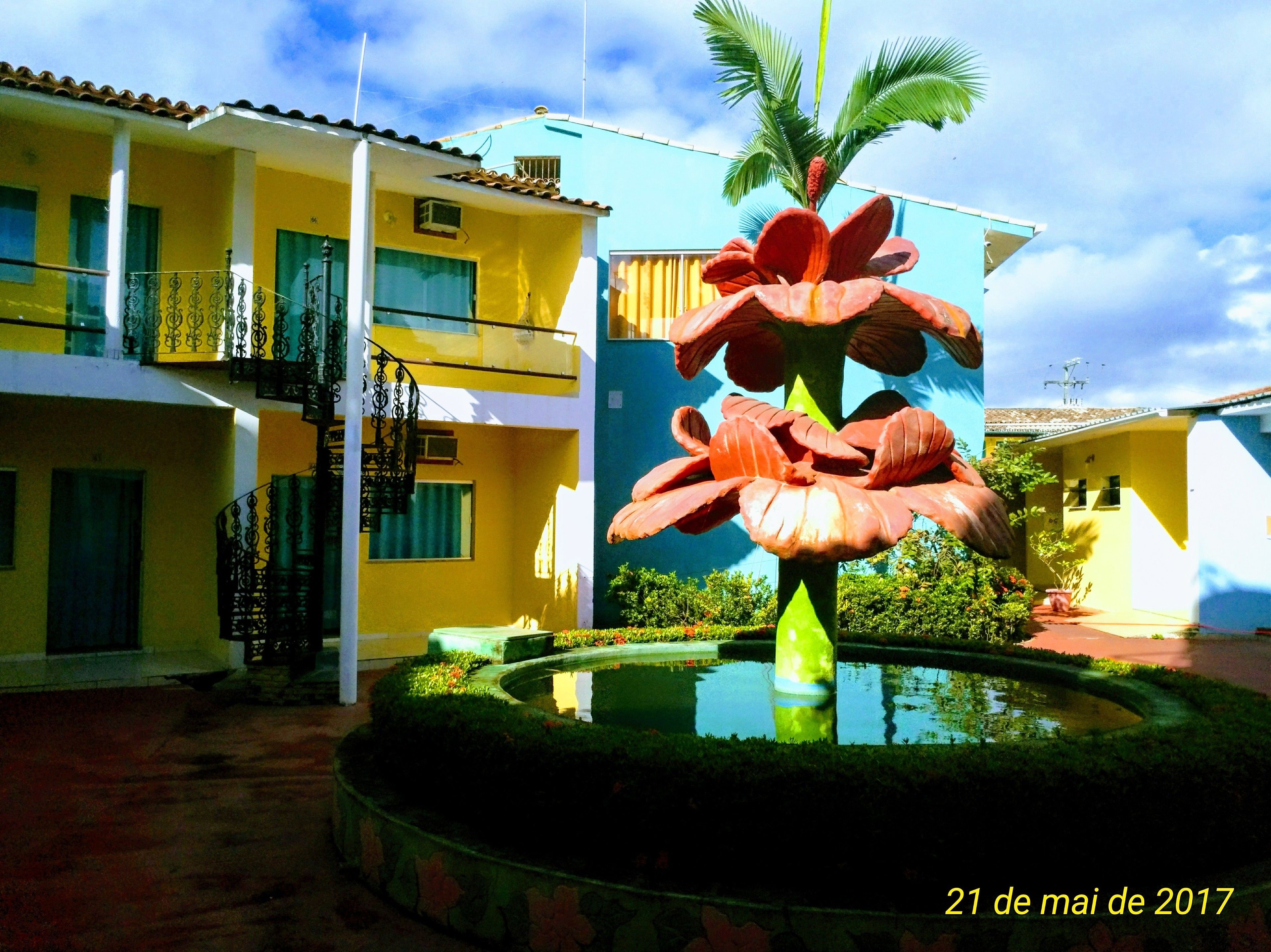 A courtyard with a large flower sculpture, a pool, and a building with balconies and a blue facade.