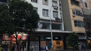 A multi-story building with numerous air conditioning units, a visible storefront with signage, and a tree in the foreground. - Rio Habitat Posto 3 Copacabana (Rio de Janeiro)