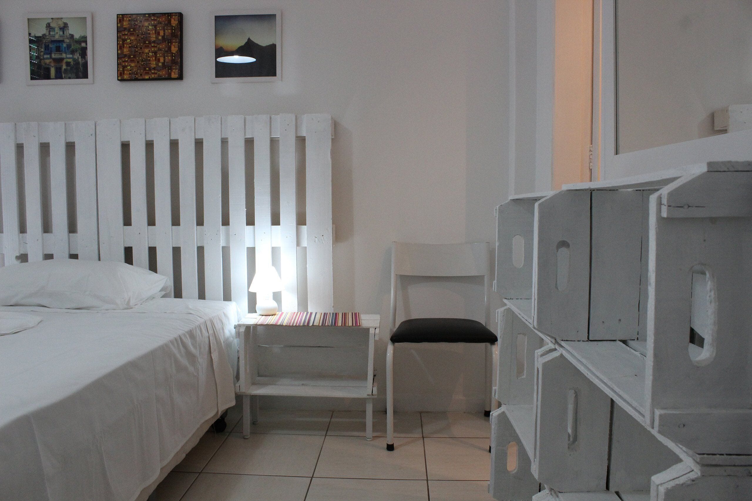 A bedroom with a white bed, a small bedside table with a lamp, a chair, and a dresser.