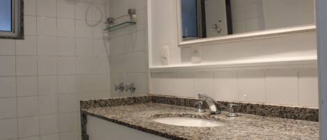 Un baño con lavamanos de encimera de granito, espejo y repisa de vidrio.