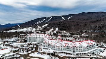 Un hotel grande de varios pisos con techo rojo, rodeado de carreteras y montañas cubiertas de nieve.