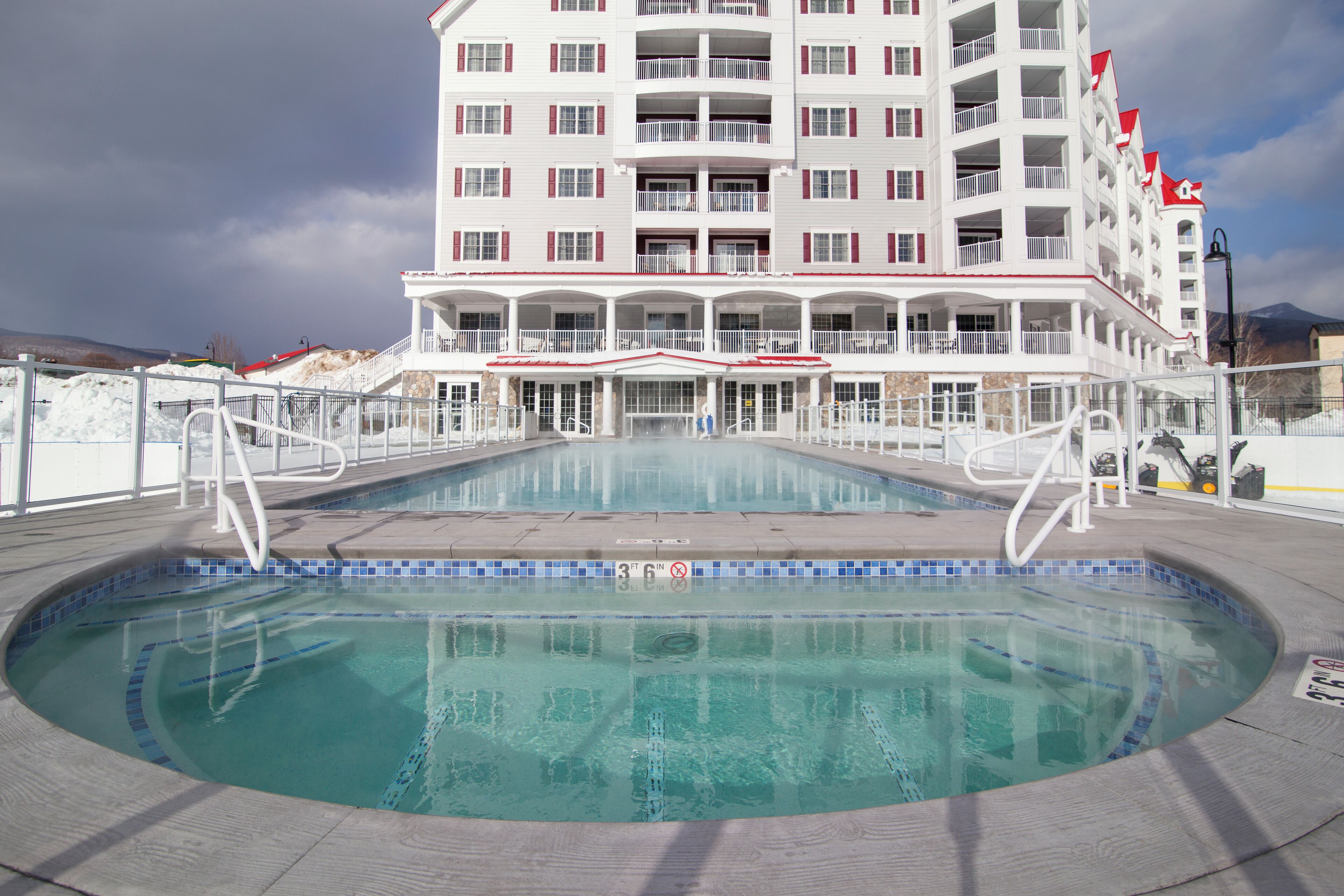 A hotel with a swimming pool, multiple balconies, and a view of the mountains.