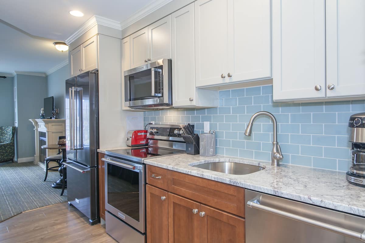 A modern kitchen with stainless steel appliances, white cabinets, and a blue tiled backsplash.
