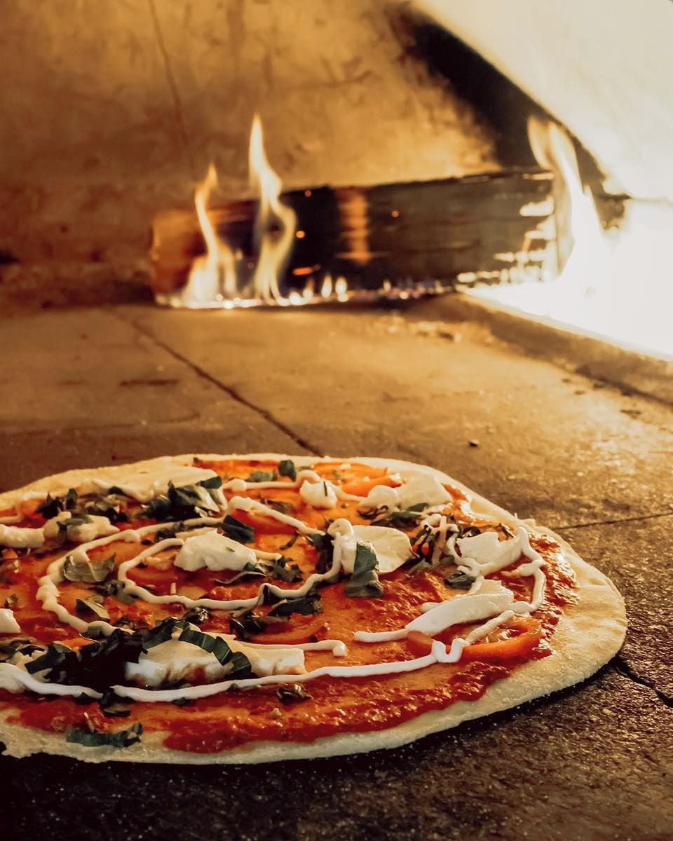 Une pizza cuite dans un four à bois, avec des flammes apparentes.