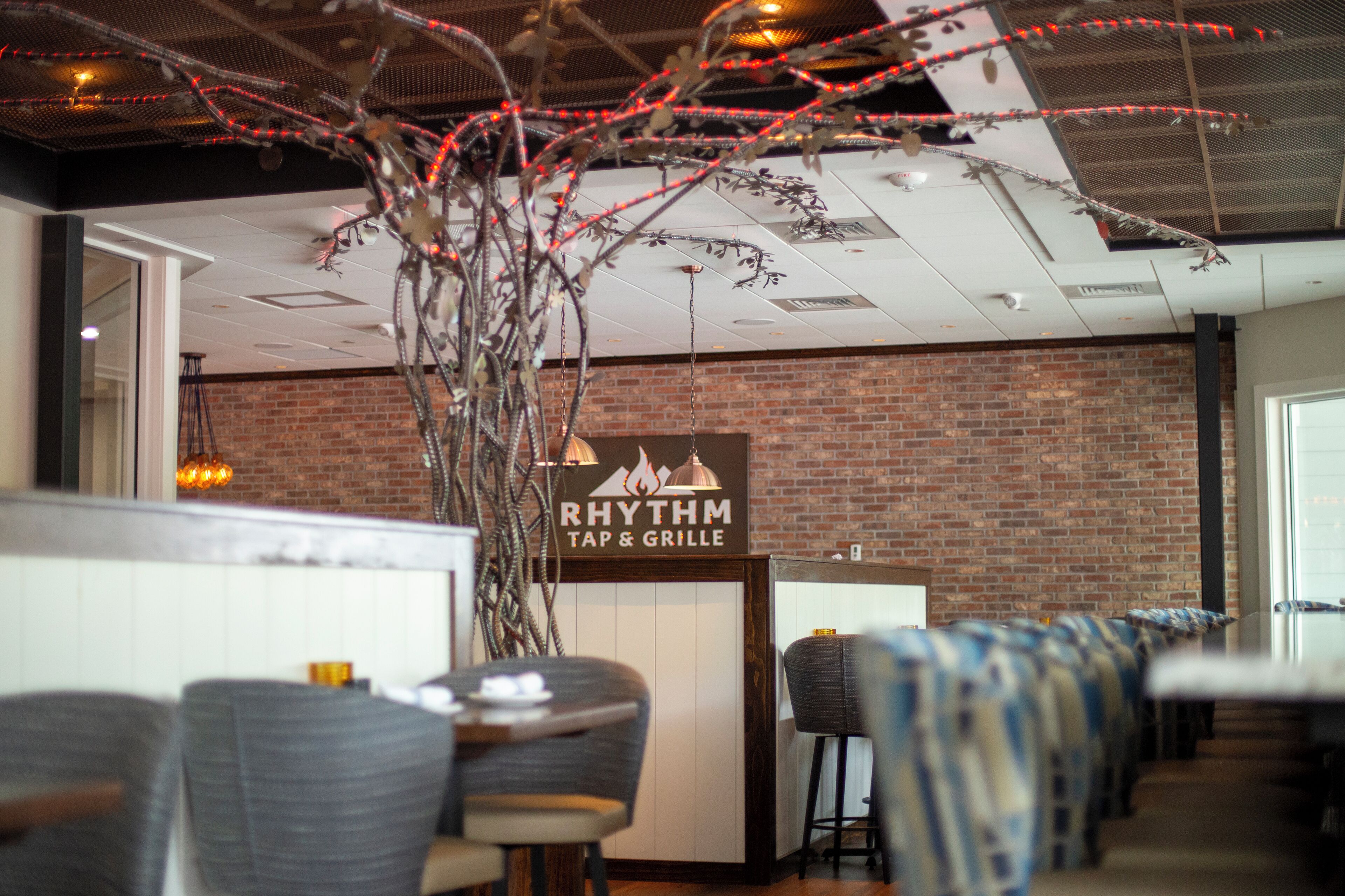 Een restaurantinterieur met een bakstenen muur, een bord met de tekst 'RHYTHM TAP & GRILLE' en rijen barkrukken.