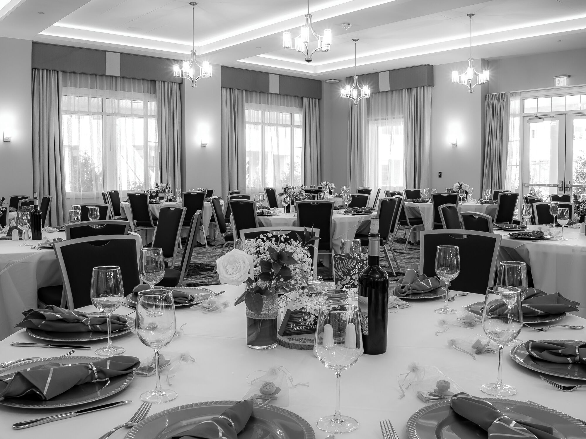 A large banquet hall with multiple tables set for dining, featuring chandeliers, curtains, and a view of the outdoors.