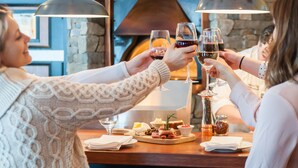 Un grupo de personas brindando con copas de vino en una mesa con una variedad de quesos, embutidos y condimentos.