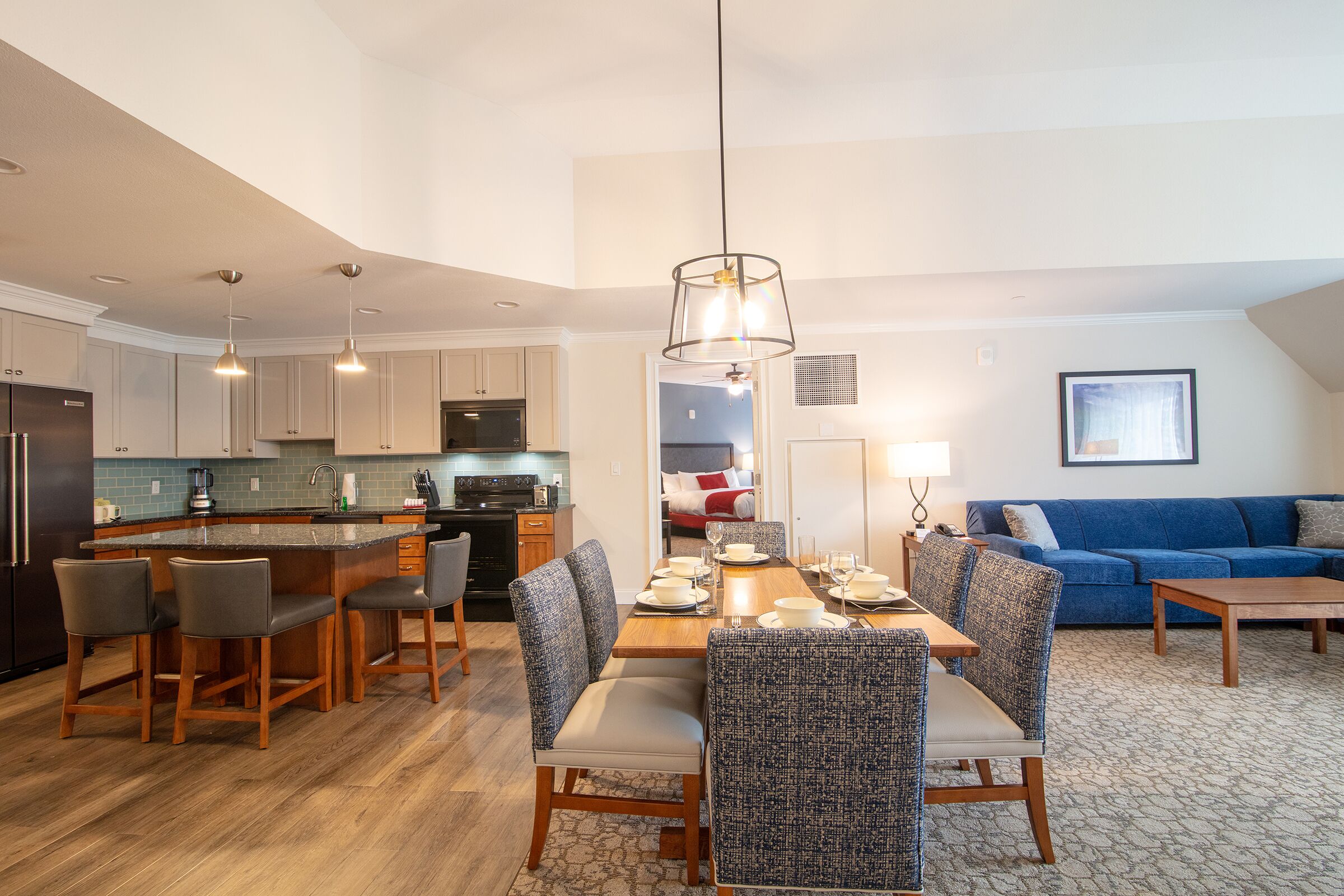 A modern kitchen with a central island, dining area with chairs, and a living room with a sofa and coffee table.