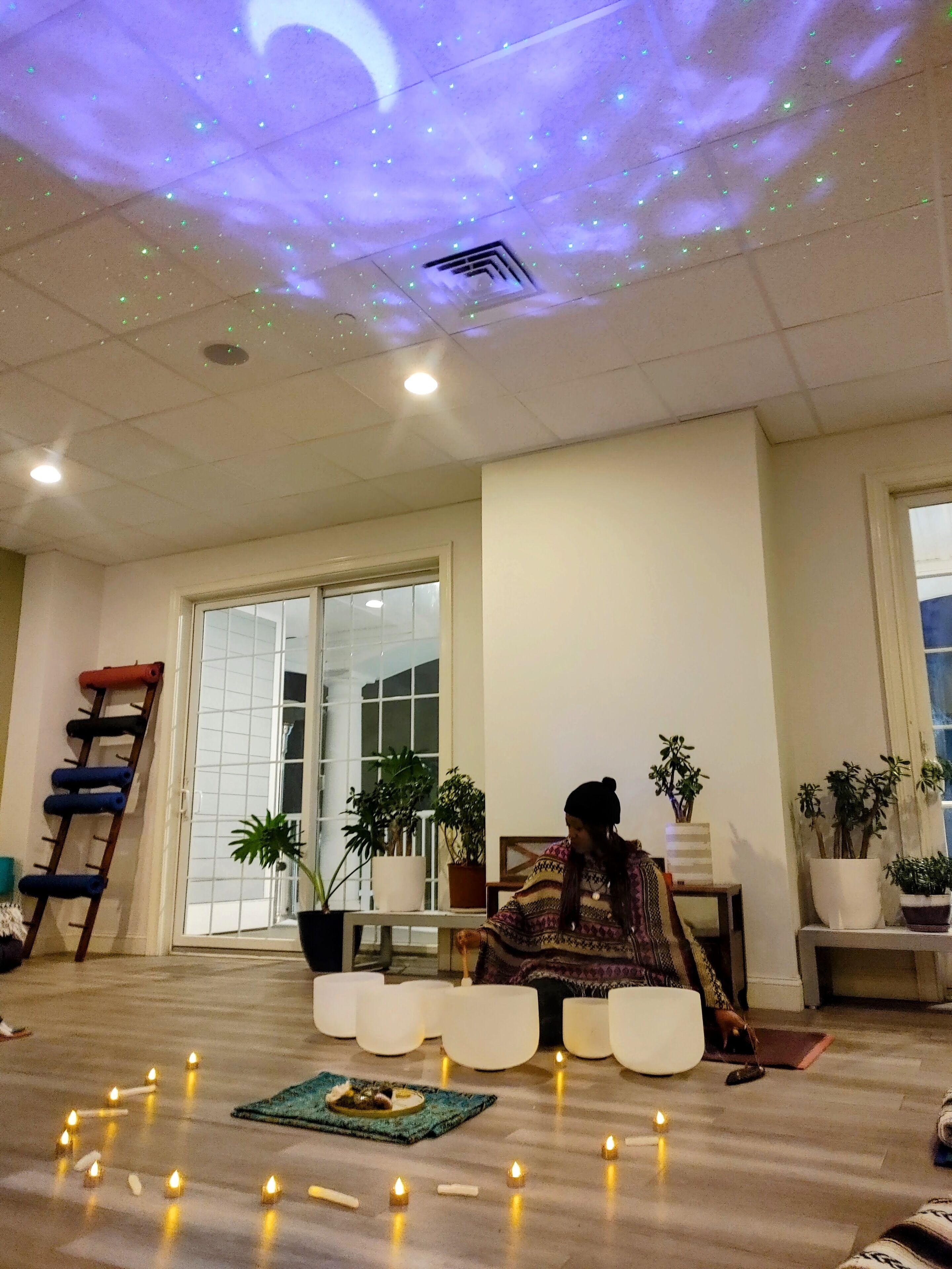 Una habitación con proyección en el techo, una escalera de madera, plantas en macetas y velas en el suelo.