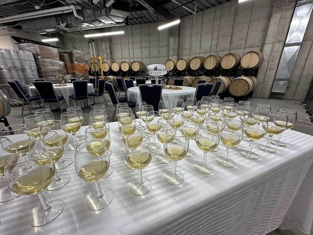 A wine tasting event with multiple tables set up for guests, surrounded by wine barrels.