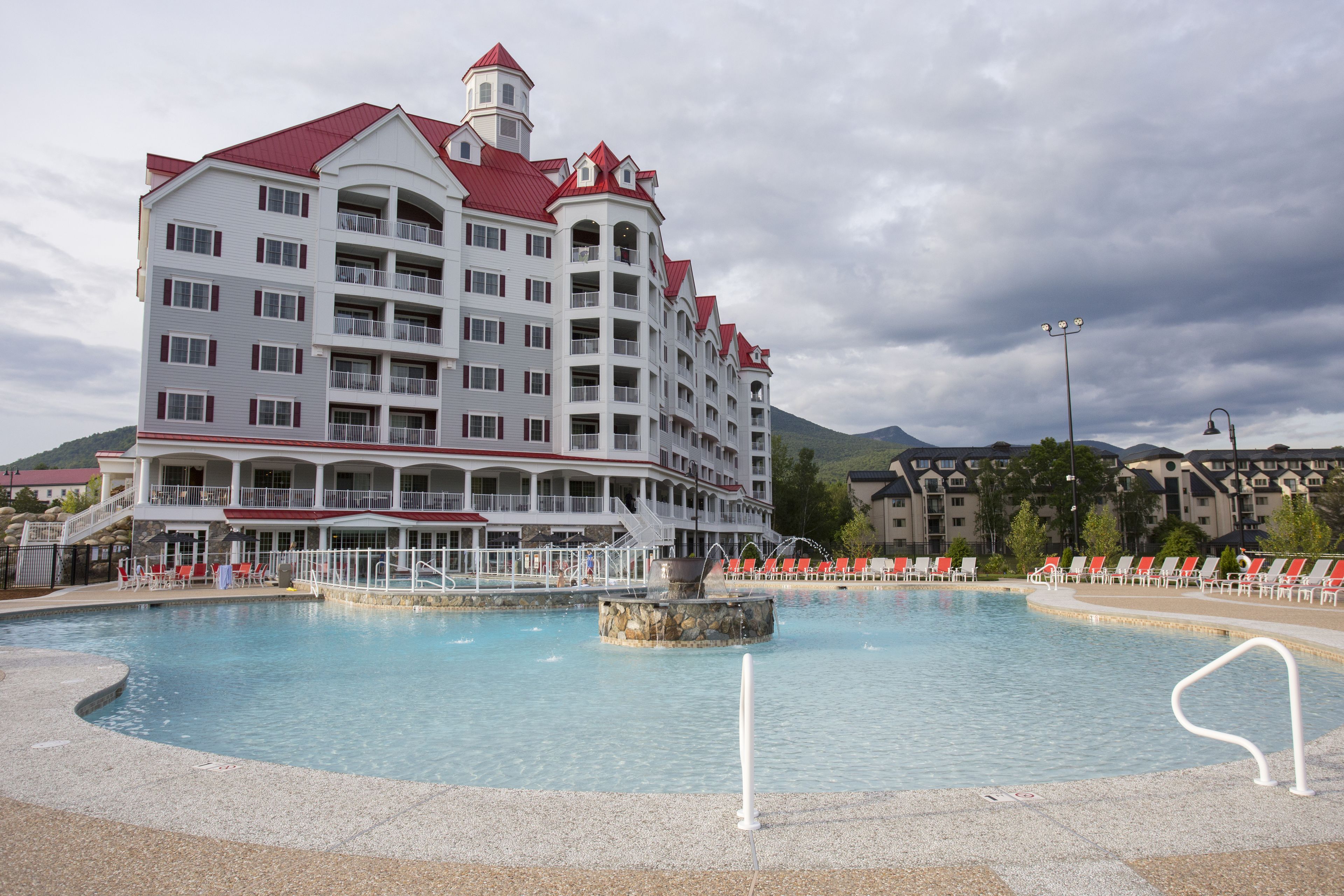 Un hotel con una piscina amplia, varios balcones y techo rojo.