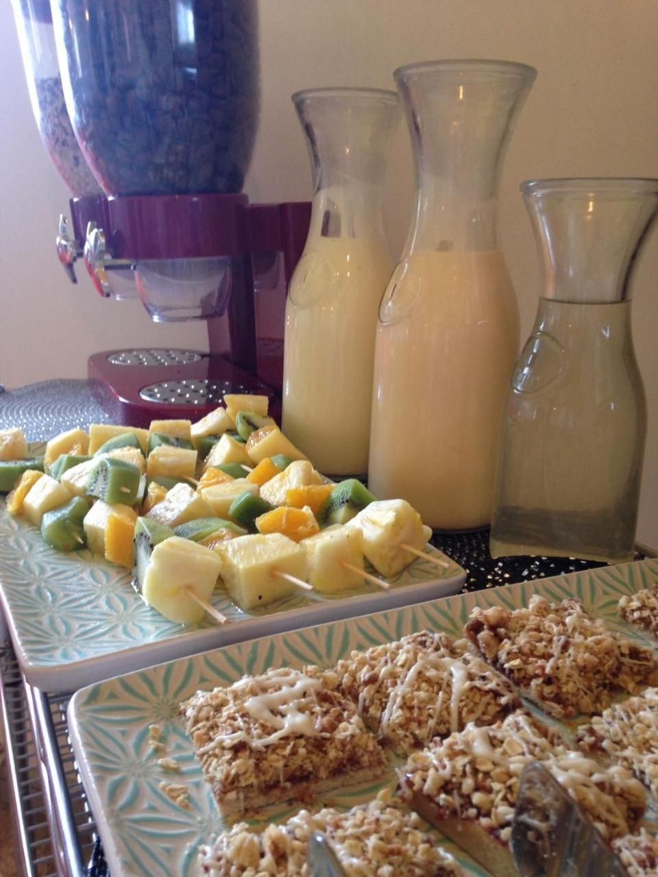 A buffet table with fruit skewers, a bottle of milk, and a plate of granola bars.