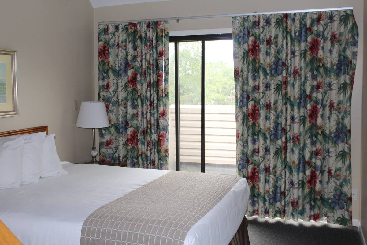 A hotel room with a bed, a nightstand, a lamp, and floral curtains.