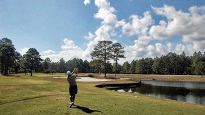 Un campo de golf con un estanque, árboles y cielo despejado.