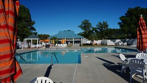 Zona de piscina con sillas de descanso, sombrillas y un pabellón.