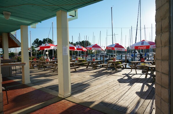 A covered outdoor area with picnic tables and red umbrellas, likely a marina or dockside restaurant.