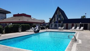 Une piscine rectangulaire à l’eau d’un bleu limpide, entourée d’une terrasse en béton. On y trouve des chaises longues et une table.