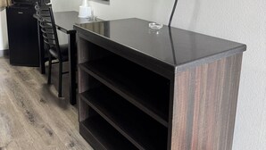 Une chambre moderne équipée d’un téléviseur à écran plat fixé au mur, d’un bureau en bois foncé avec un plateau en verre, d’un fauteuil de bureau noir, d’un four à micro-ondes et d’un petit réfrigérateur.