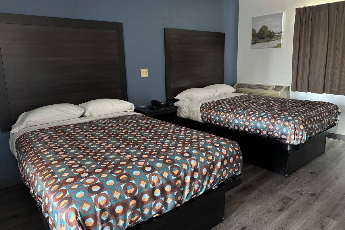 A hotel room with two beds, a nightstand, a telephone, and a painting on the wall.