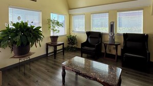 Une pièce avec un plancher en bois, une table basse en marbre, deux chaises noires, une plante en pot et un tableau accroché au mur.