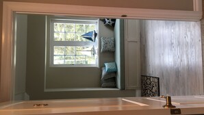 A bathroom with a large mirror, a window with a view of trees, and a wooden floor. - Alaska SeaScape Lodge (Kenai)