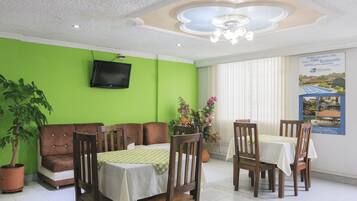 A dining area with green walls, a television mounted on the wall, and a poster advertising a tennis restaurant.