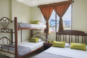 Habitación de hotel con literas, dos almohadas verdes con la marca 'Ayenda Hotels', una ventana con cortinas y vistas a un paisaje urbano.