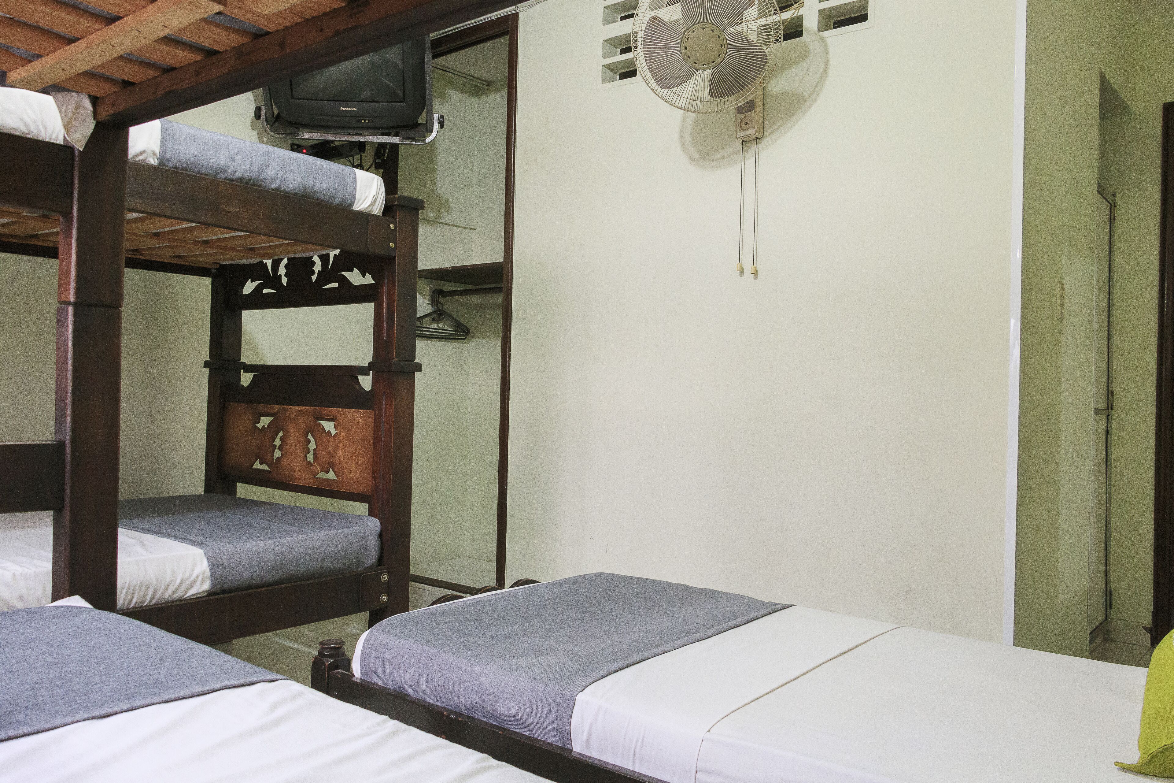 A dormitory room with bunk beds, a television, and a wall-mounted fan.