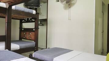 A dormitory room with bunk beds, a television, and a wall-mounted fan.