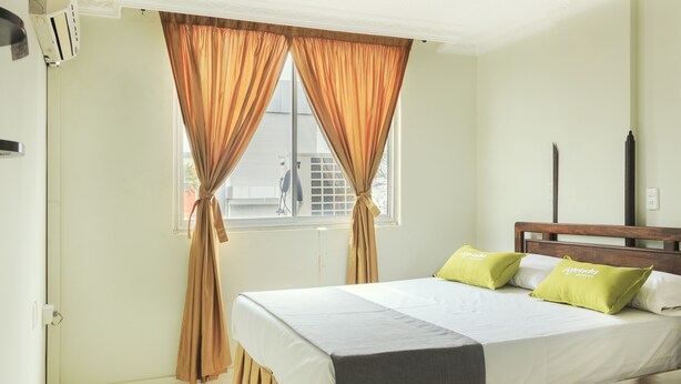 A bedroom with a bed, curtains, a window, and a wooden headboard.