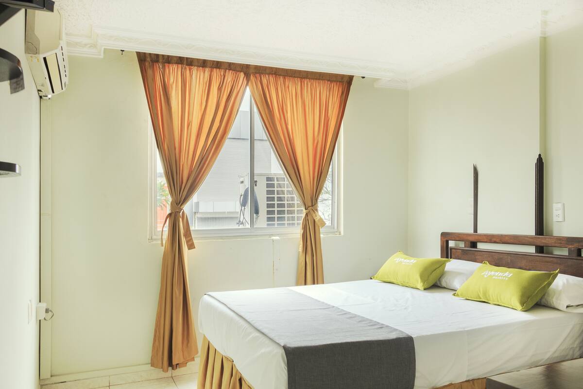 A bedroom with a bed, curtains, a window, and a wooden headboard.