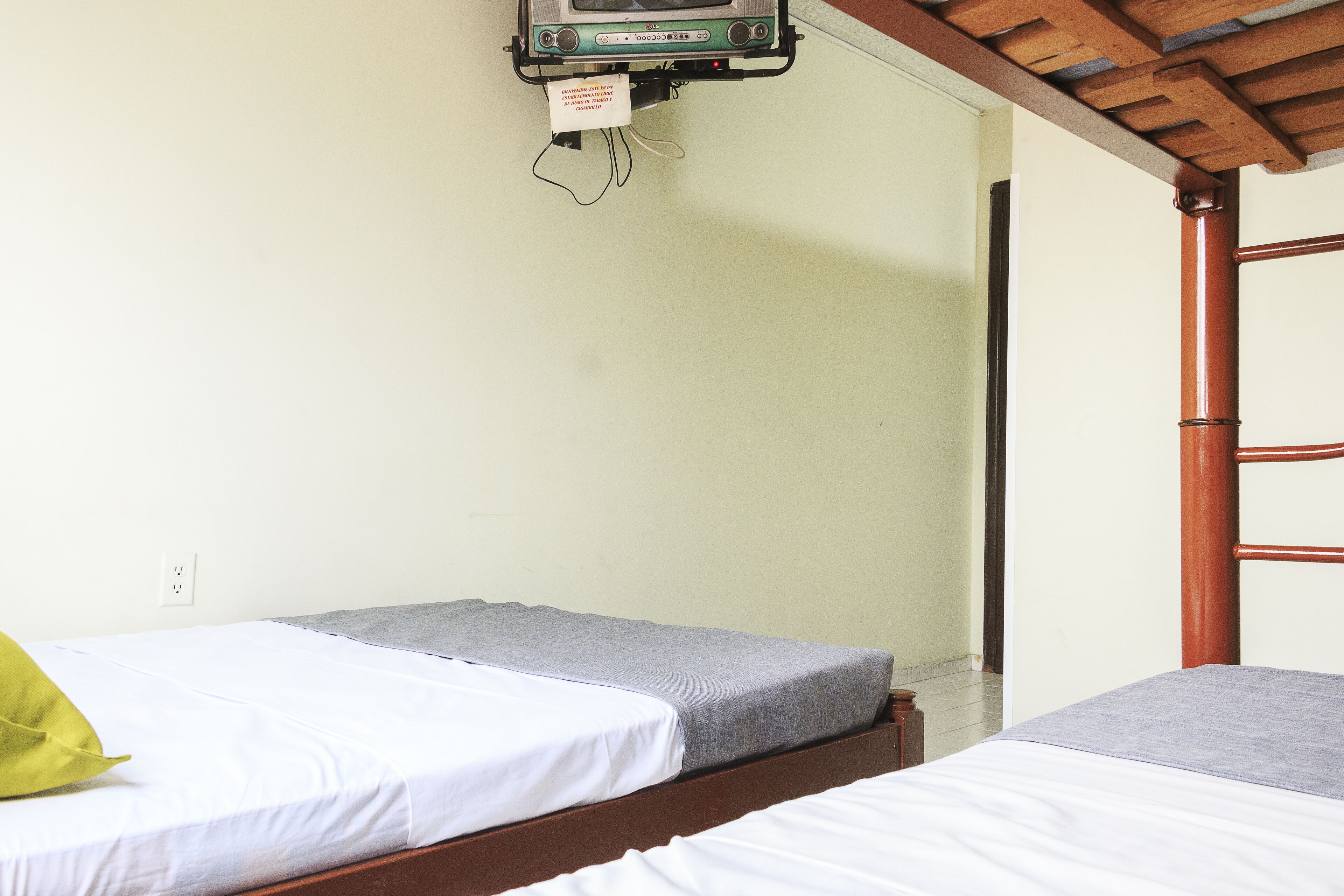 A room with two single beds, a wooden ceiling, and a small TV mounted on the wall.